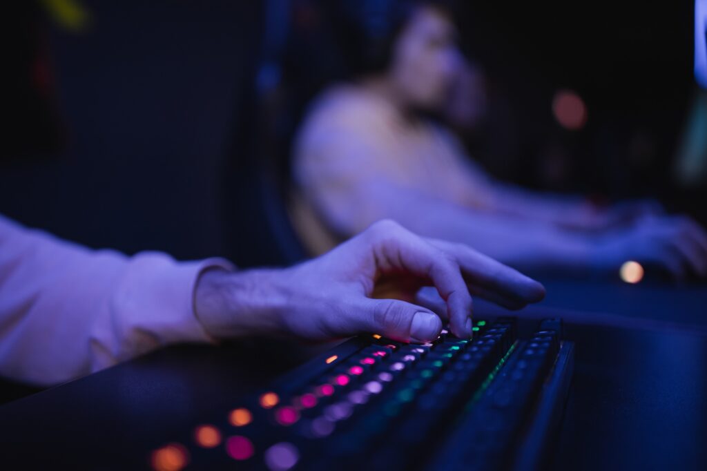 Cropped view of gamer using keyboard with lighting in cyber club